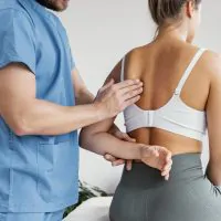 vista-lateral-do-terapeuta-osteopatico-masculino-verificando-o-osso-da-escapula-de-uma-paciente-do-sexo-feminino